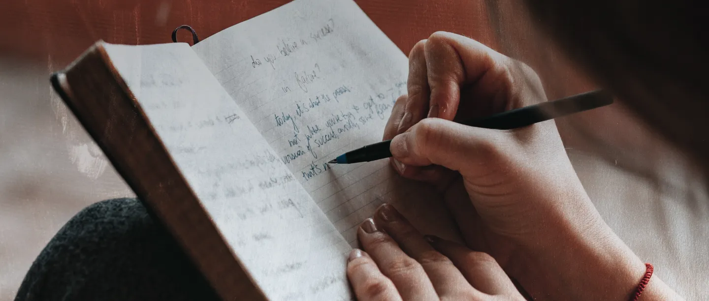 The banner image is a close up of hands writing in a notebook. A black pen is held in the right hand. The hands appear to belong to a young woman. 
