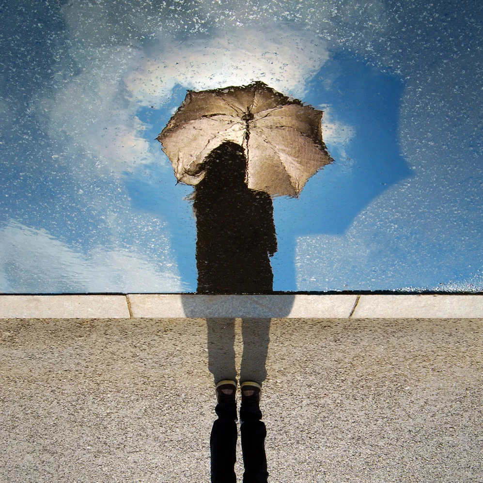 An abstract image of the silhouette of a woman with long hair holding an umbrella. Around the umbrella a rain storm and clouds swirl ominously.