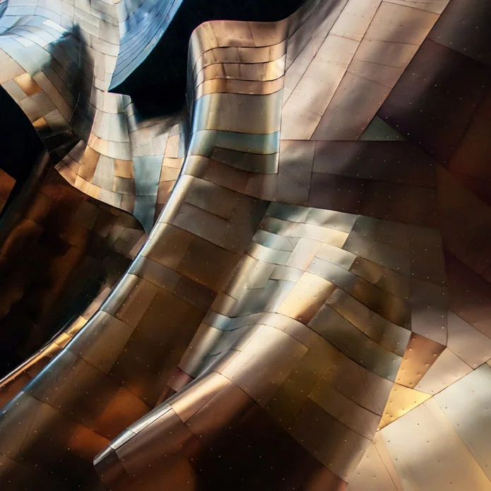 Abstract photograph of a metallic sculpture. The metal looks folded with squares of different silver and brown tones. 
