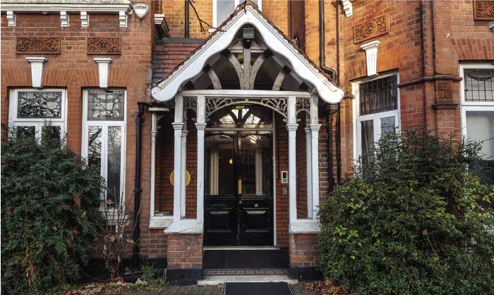 A photograph of the front of the British Psychotherapy House on Mapesbury Road in North London. The house is red brick with a black front door. 