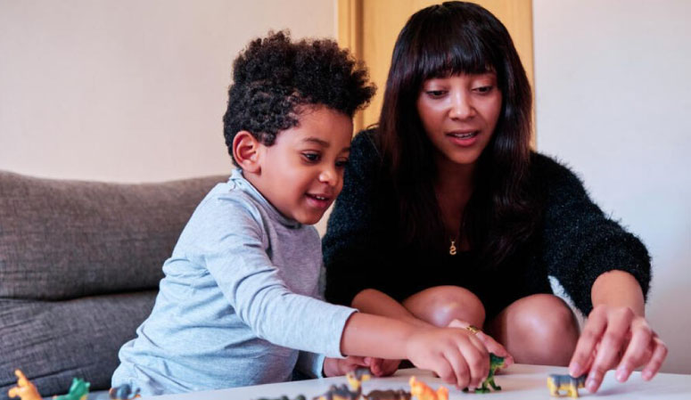 Child and Therapist sitting at a table playing with dinosaur toys.